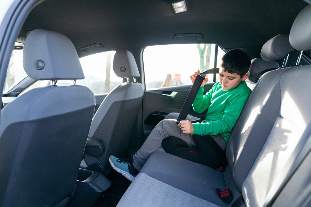 Young boy in back seat fastening seat belt on booster, preparing for a safe family car trip with responsible travel routine