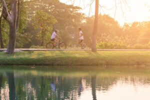 Cyclist and jogger on greenway along a lake as the sun sets.